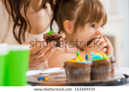 Cropped image of mother holding cupcake with girl eating cake at birthday party