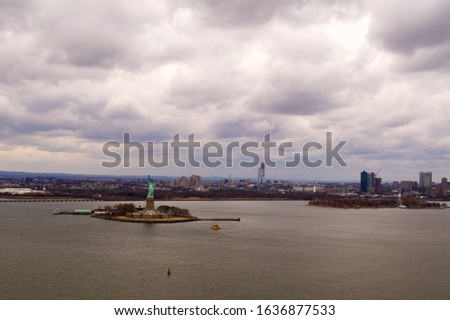 An aerial view over the Upper Bay waters with the Statue of Liberty in the background and it is a cloudy day. I flew over from Bush Terminal Park in Brooklyn, New York