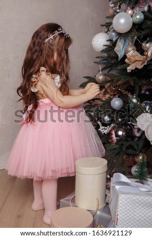 Little long-haired brown-haired woman in a pink dress decorates the Christmas tree