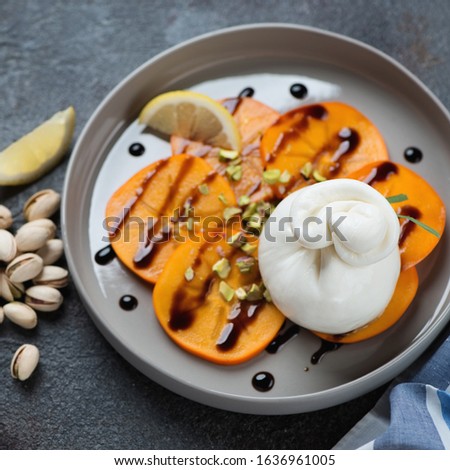 Close-up of burrata cheese, persimmon and pistachios salad served on a grey plate, selective focus, studio shot