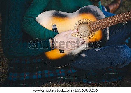 Young couple in love camping tourists sitting by a campfire against a tent in the woods playing guitar