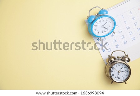 Alarm clocks with calendar on yellow background.