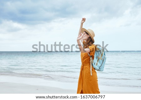 woman near the sea with a backpack on her back raises her hand up