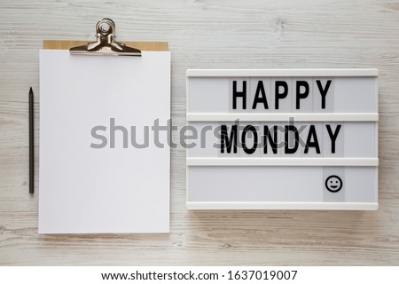 'Happy monday' words on a lightbox, clipboard with blank sheet of paper on a white wooden background, top view. Overhead, from above, flat lay. Close-up.