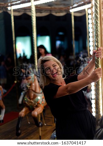 Portrait of a fun attractive blonde woman on bright carousel at night in the city of Florence. Concept of travel, destination, summer, vacation, fun.