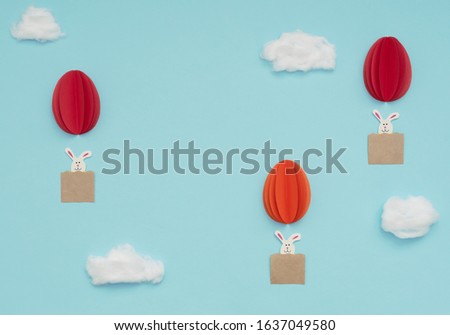 Easter egg hot air balloons made of paper with bunnies fly in blue sky with cotton clouds background. Happy Easter holiday concept. Greeting card. Flat lay style with copy space.