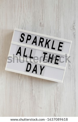 'Sparkle all the day' words on a modern board on a white wooden surface, top view. Overhead, from above, flat lay. 