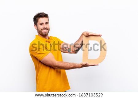 young handsome man excited, happy, joyful, holding the letter D of the alphabet to form a word or a sentence.