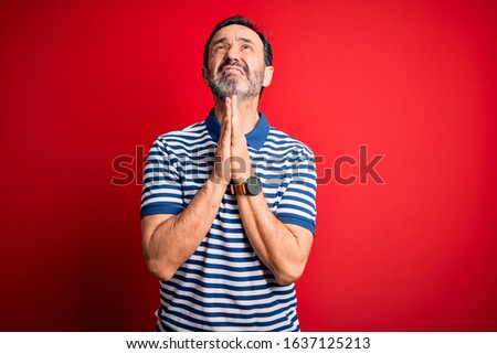 Middle age hoary man wearing casual striped polo standing over isolated red background begging and praying with hands together with hope expression on face very emotional and worried. Begging.