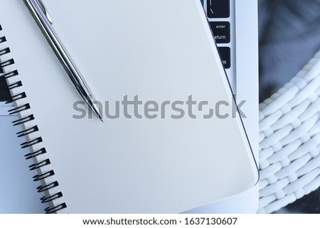 Mockup, blank white open notebook with ballpoint pen on laptop computer on table, top view, close up