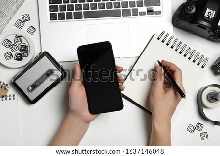 Journalist with smartphone working at white table, top view