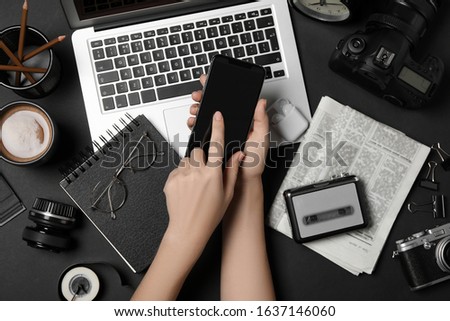 Journalist with smartphone working at black table, top view