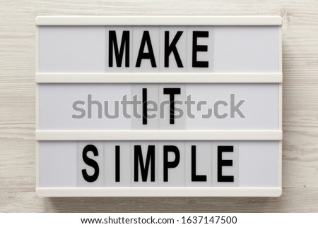 'Make it simple' words on a lightbox on a white wooden background, top view. Overhead, from above, flat lay. Close-up.