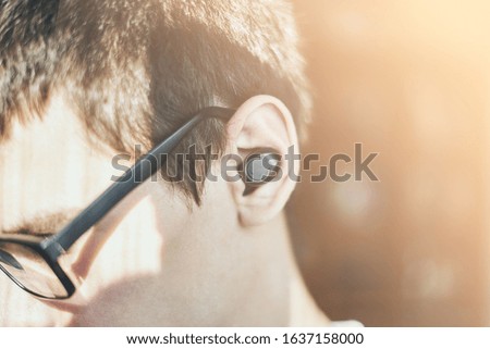Young man in glasses listening to music, wireless earphone in ear soft focus