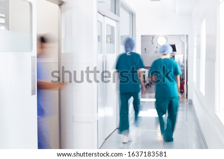 Motion Blur Shot Of Medical Staff Wearing Scrubs In Busy Hospital Corridor