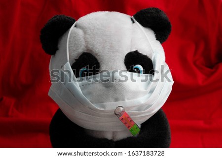 A toy panda in a medical mask with a thermometer sits on a red background. Coronavirus treatment concept