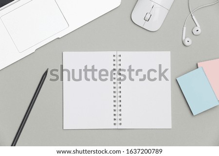 Blank notepad over laptop and headphones on gray office table
