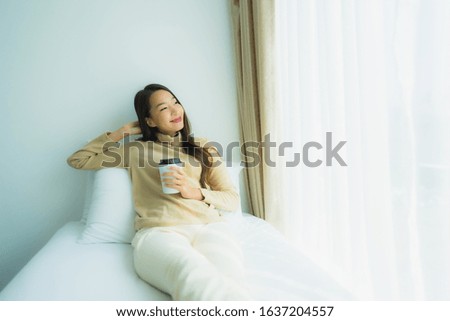 Young asian woman with coffee cup on bed in bedroom interior