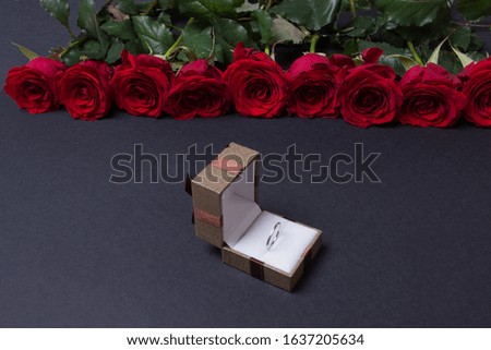 Bouquet of red roses and opened brown jewellery box on black background, side wiew.