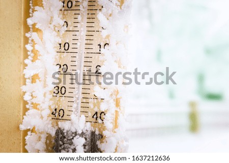 Frozen Outdoor Thermometer on Wall with Blurred Winter Landscape Covered with Snow on Background