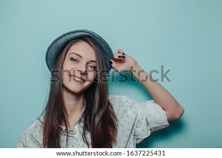 Pretty woman in a gray hat with long hair on the blue background. Smiling woman with white teeth in white shirt.