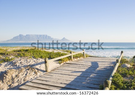 Table Mountain - the world famous landmark in Cape Town, South Africa. Picture taken on a clear Winters day from the Blouberg Strand beach. A wooden bridge over a sanddune is in the foreground.