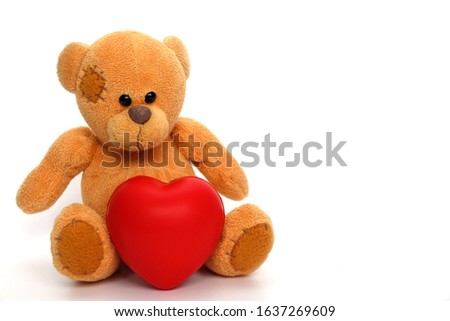 Teddy bear with a red heart on a white background. A teddy bear holds a big heart in his hands. February 14, Valentines Day. Romantic concept with place for text.