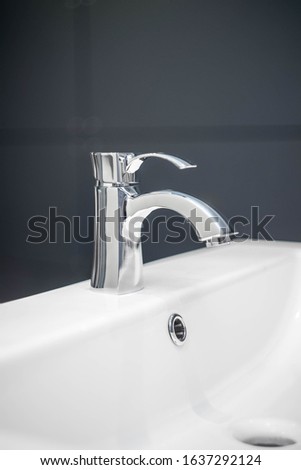 The mixer is mounted on a ceramic sink. Modern water tap. Dark background. studio shot.