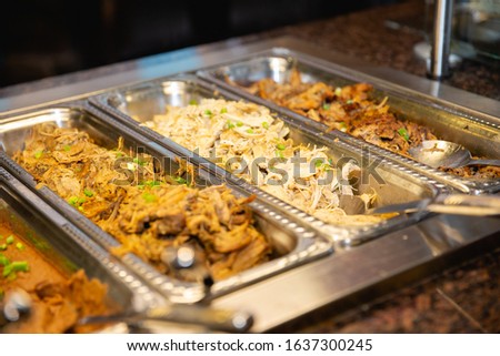 Buffet line for taco bar with various meats, rice, and beans