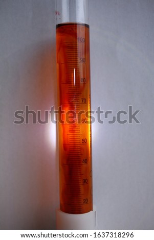 A ray of light illuminates the surface of a measuring cylinder with a red liquid substance.