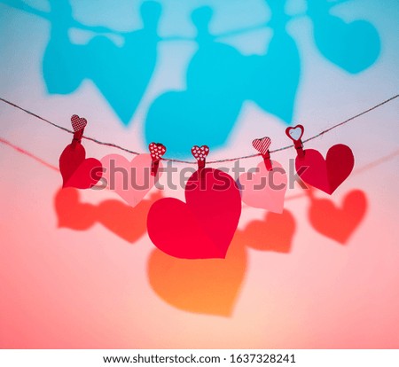 Paper hearts of red clothespins with a heart on a rope with a shadow. Valentine's Day love. blue-pink background. copy space
