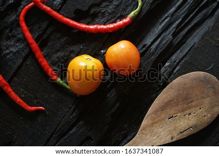 Two tomatoes and chili on a black wooden table