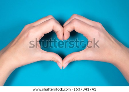Closeup point of view photography of two beautiful manicured female hands making heart shape gesture isolated on bright blue background. 