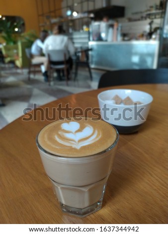 Glass of flat-white coffee served on the tabletop, blurry cafe interior is on background