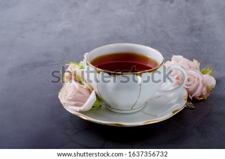 Romantic Tea time backdrop with vintage white porcelain tea cup, gentle pink roses on a dark gray background.