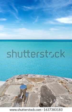 Stone jetty with an empty mooring bollard and turquoise seascape with blue sky and clouds