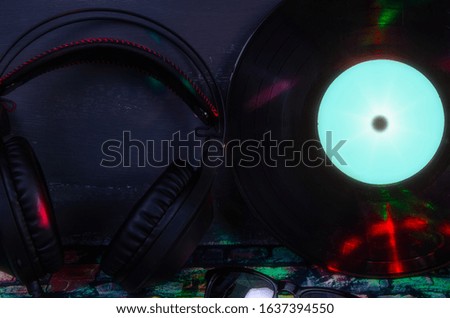 Large overhead headphones for DJ music, sunglasses and an old vinyl record in dark colors and colored rays on a dark background. DJ's day. Horizontal frame