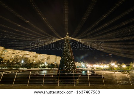 City Christmas tree decorated with balls and garlands stands in the center against the background of residential buildings