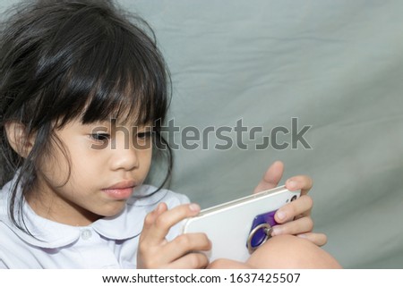 An Asian girl is playing with a smartphone alone without a parent.