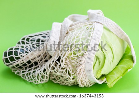 string bag with cabbage and courgette on green background