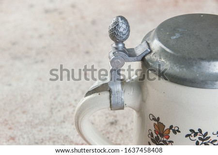 Collectible vintage ceramic beer mug with pewter lid and colorful rooster on a concrete background. Copy space for text.
