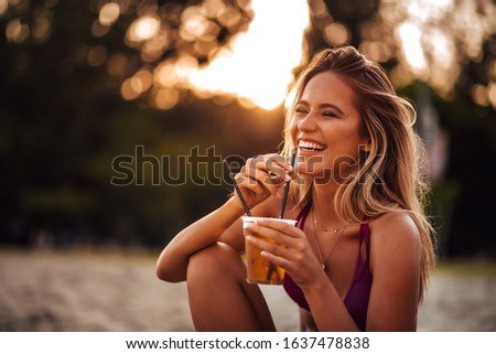 Close-up portrait of a beautiful happy young woman drinking on a beach. Summer vacation concept.