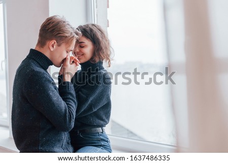 Cute young couple embracing each other indoors near the window.