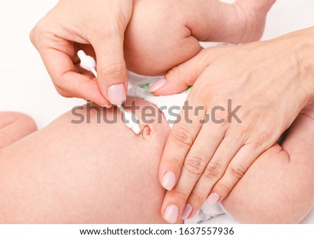 Mother or pediatrician uses a cotton swab to clean navel (belly button) of newborn baby wipes it with water Royalty-Free Stock Photo #1637557936