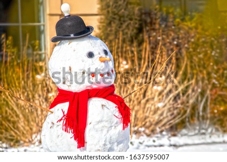 Snowman with a bright idea - torso and head of cute snowman with red scarf and bowler hat with light bulb on top in front of blurred outdoor background