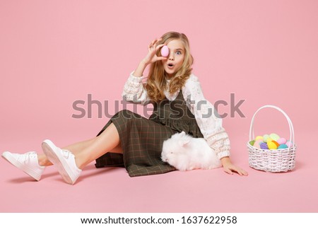Little pretty blonde kid girl 11-12 years old in spring dress hold fluffy white bunny rabbit isolated on pastel pink background children studio portrait. Childhood lifestyle Happy Easter concept