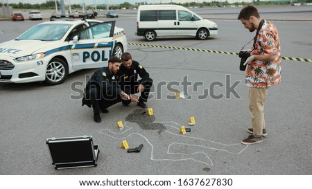 Police crime scene investigation. Two policemen working with evidence while a forensics researcher taking photographs of the body outline.