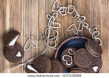 chocolate chip cookie sandwich in a clay plate on a wooden surface. hearts of wood strung on a rope. Happy Valentine's day. Nice picture. wooden background. texture.