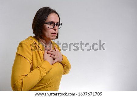 Pretty brunette woman having breath difficulties in front of white background. A young woman holding her breast in pain Royalty-Free Stock Photo #1637671705
