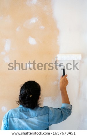 Brunette woman painting a wall on white with a paint roller. Vertical photography. Copy space